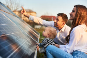 A father, mother, and toddler are sitting looking at a solar panel. They are smiling as the father points to the panel.